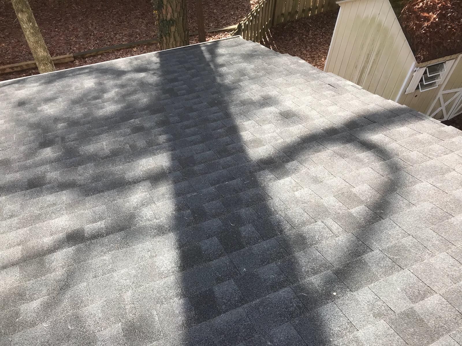Snow-covered rooftop with long tree shadows and a fence in the background