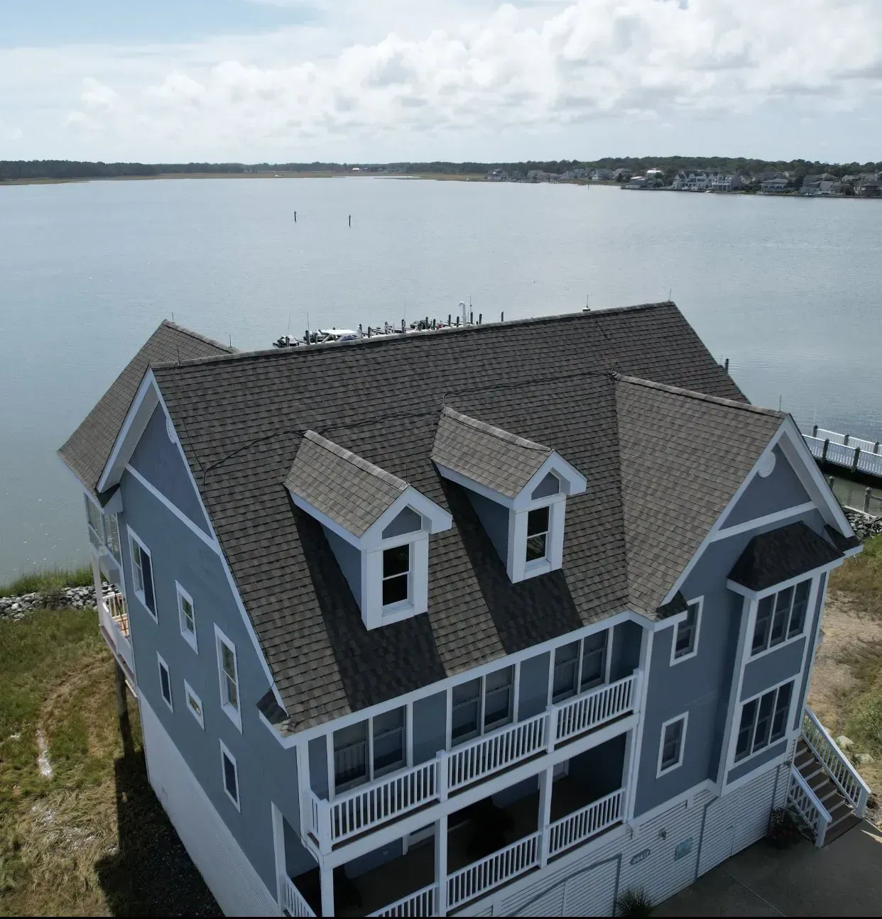 Blue lakeside house with gray roof and balconies, viewed from above over calm water