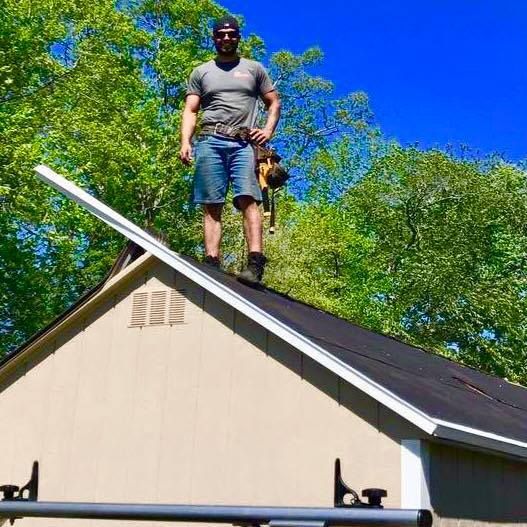 Person standing on a roof above a beige garage under a bright blue sky.