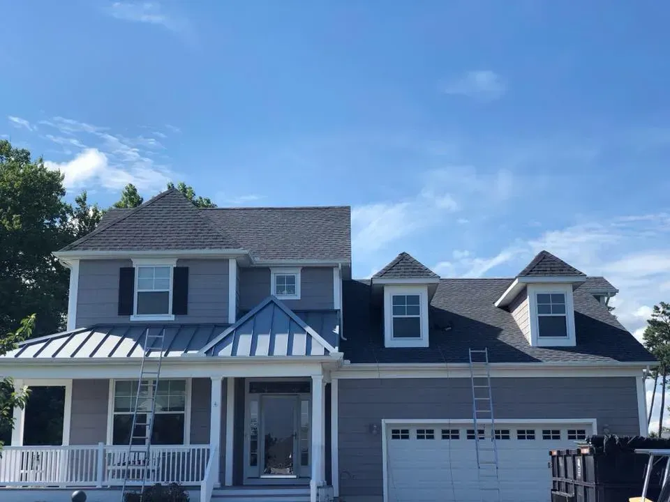 Two-story white house with blue roof and porch under a clear blue sky
