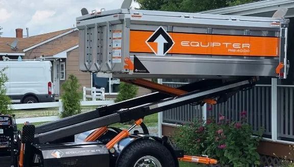 Orange dump trailer tipping up to unload in a residential driveway