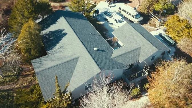 Aerial view of a gray-roofed house surrounded by trees and a driveway.