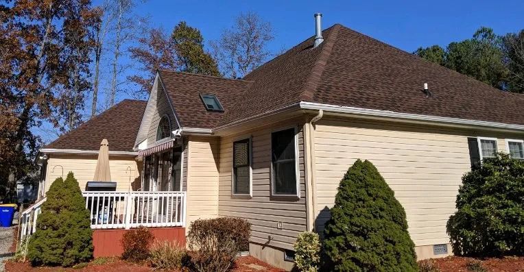 Suburban house with tan siding, dark roof, and a small white porch under a clear blue sky