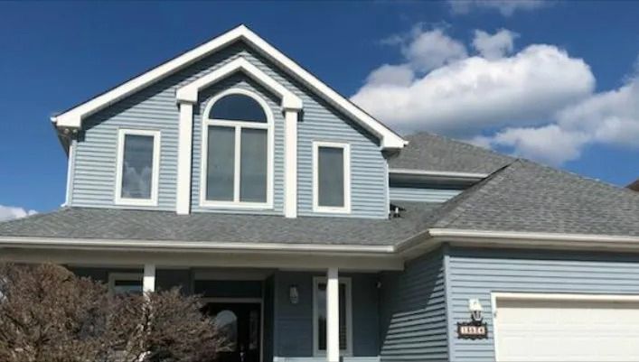Blue suburban house with white trim and a garage under a partly cloudy sky