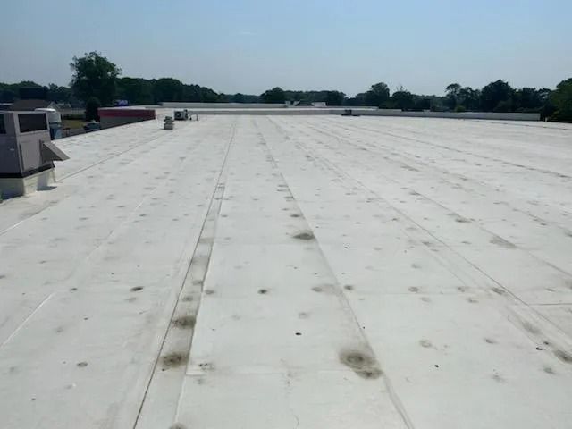 Flat white rooftop with vents and distant trees under a clear blue sky