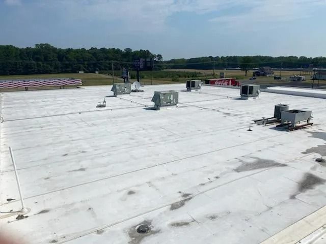 Flat white rooftop with HVAC units and vents under a clear sky, trees in the distance
