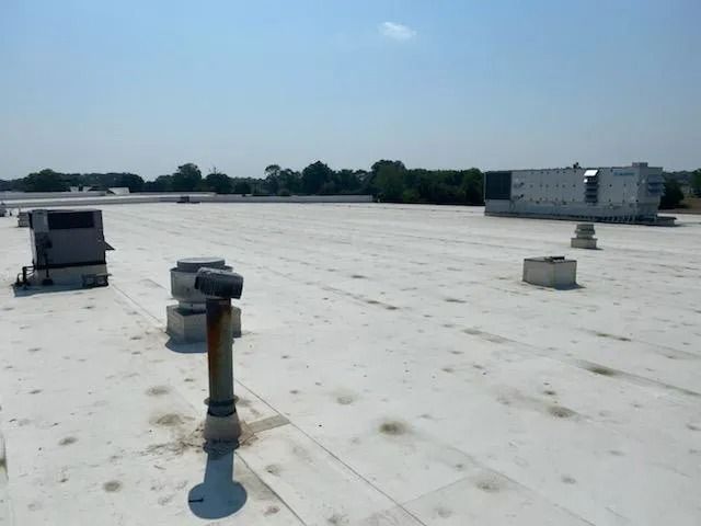 Flat white rooftop with ventilation equipment under a clear blue sky, trees and a building in the distance