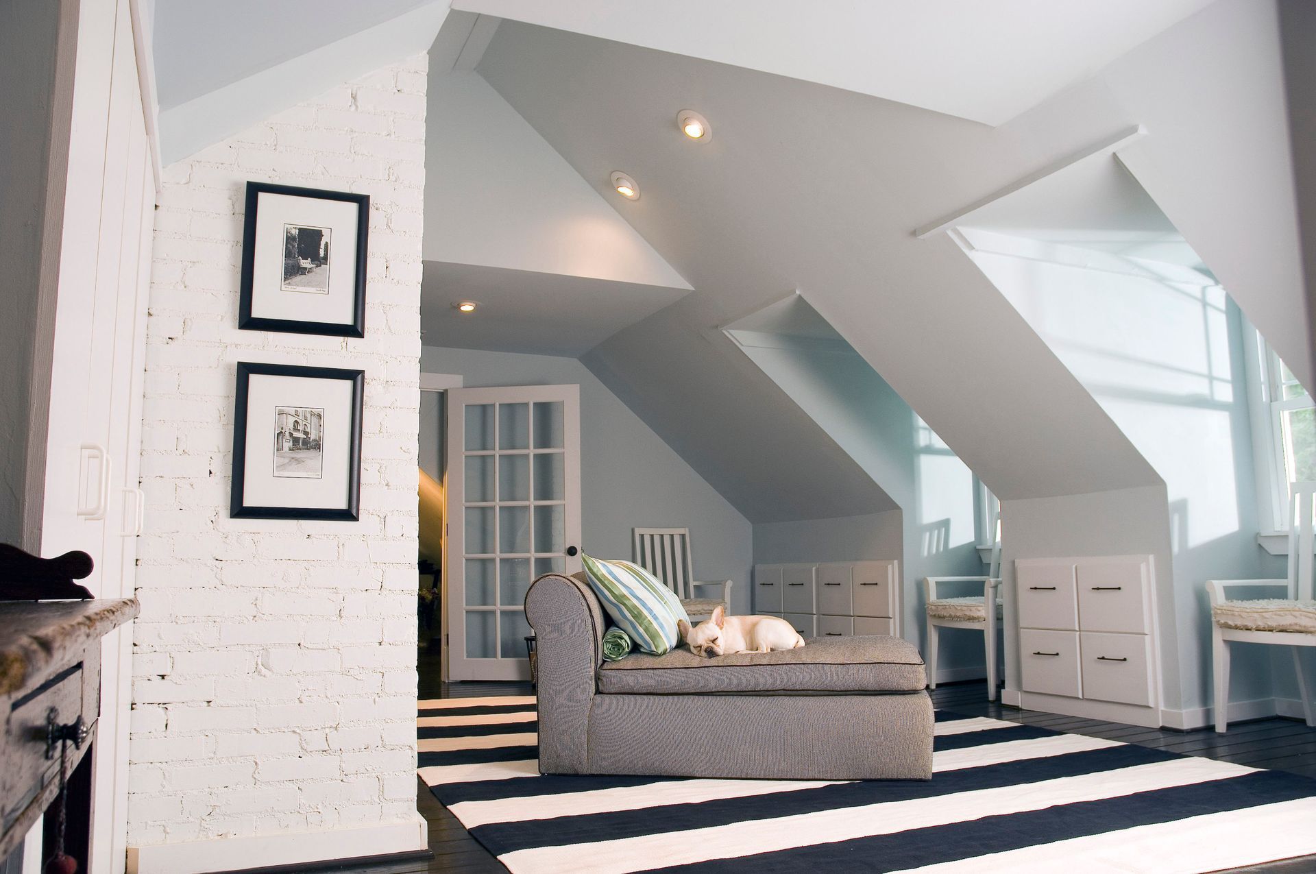 Bright attic living room with gray sofa, striped rug, white walls, and slanted skylight windows
