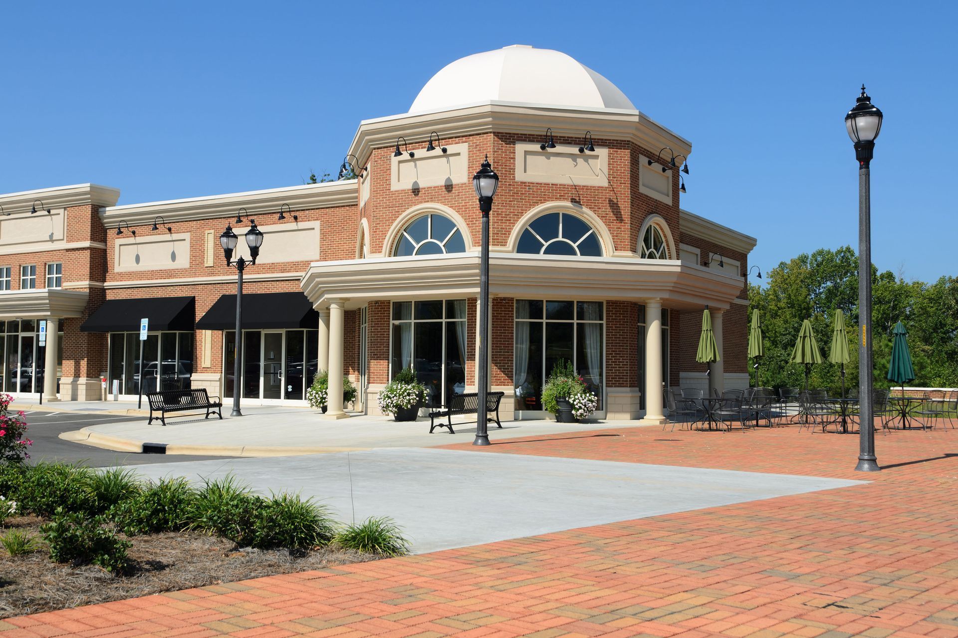 Brick building with a white dome, arched windows, and a covered entrance in a sunny plaza
