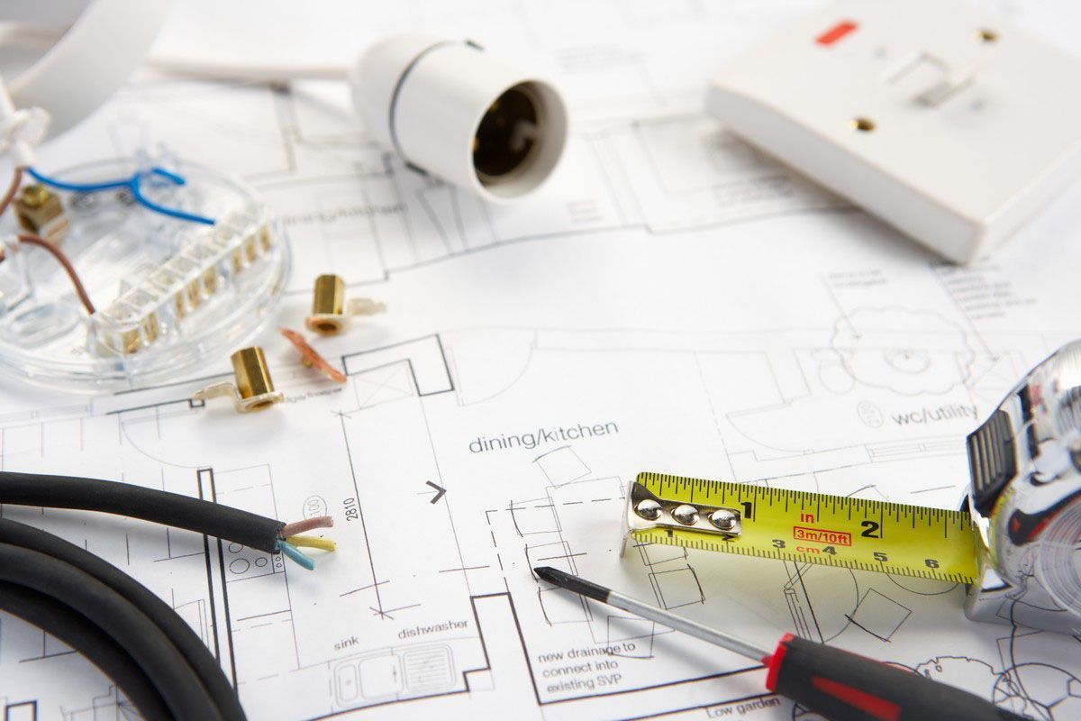 Electrical tools and wiring over a floor plan, with a tape measure and pen on a desk