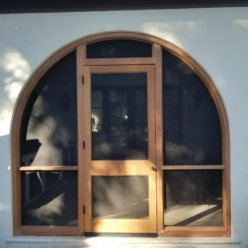 Wood-framed arched storefront door and windows with dark glass panels in a brick wall.
