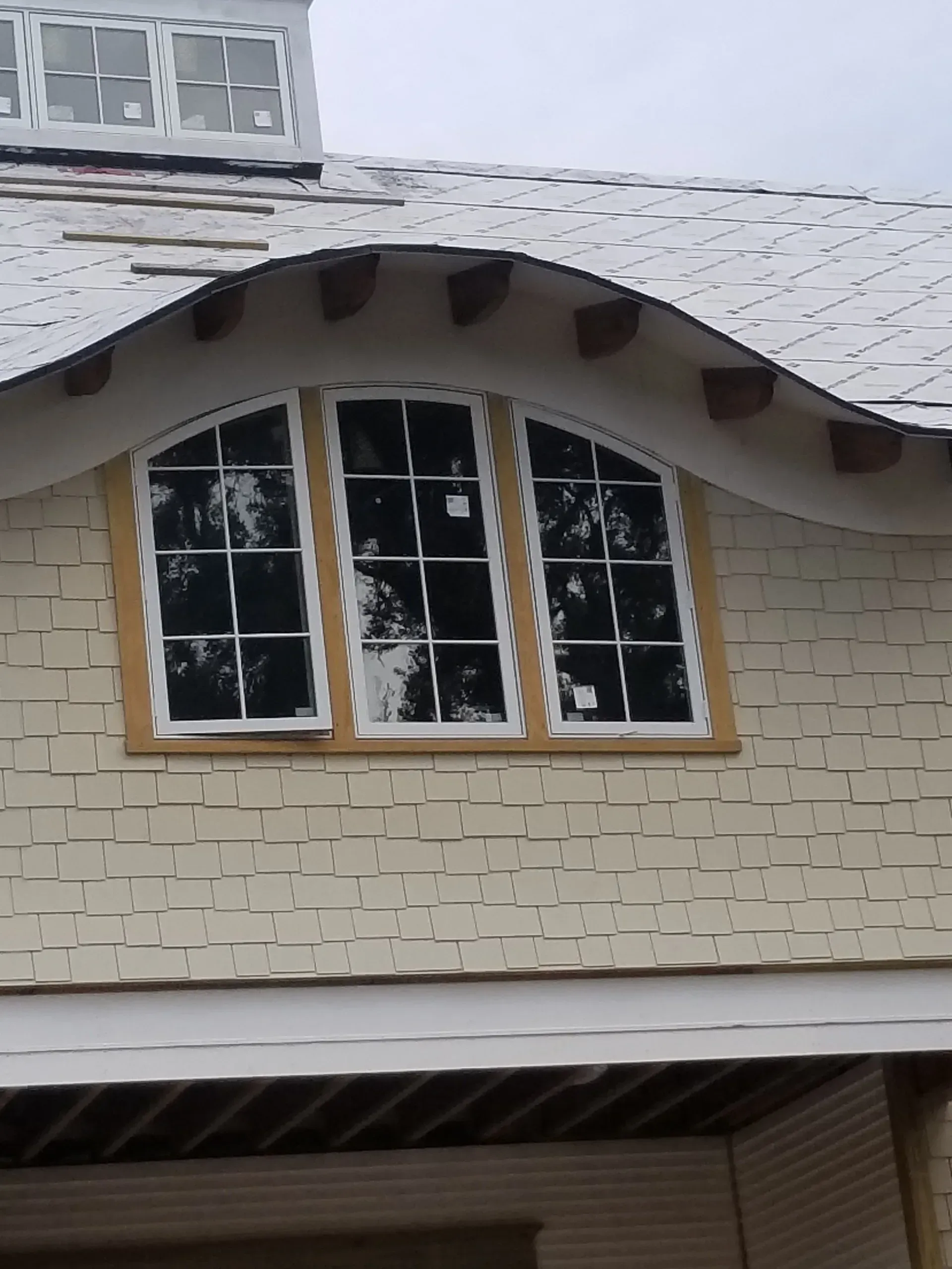 Upper-story house window with white trim and dark shutters beneath a gray shingled roof