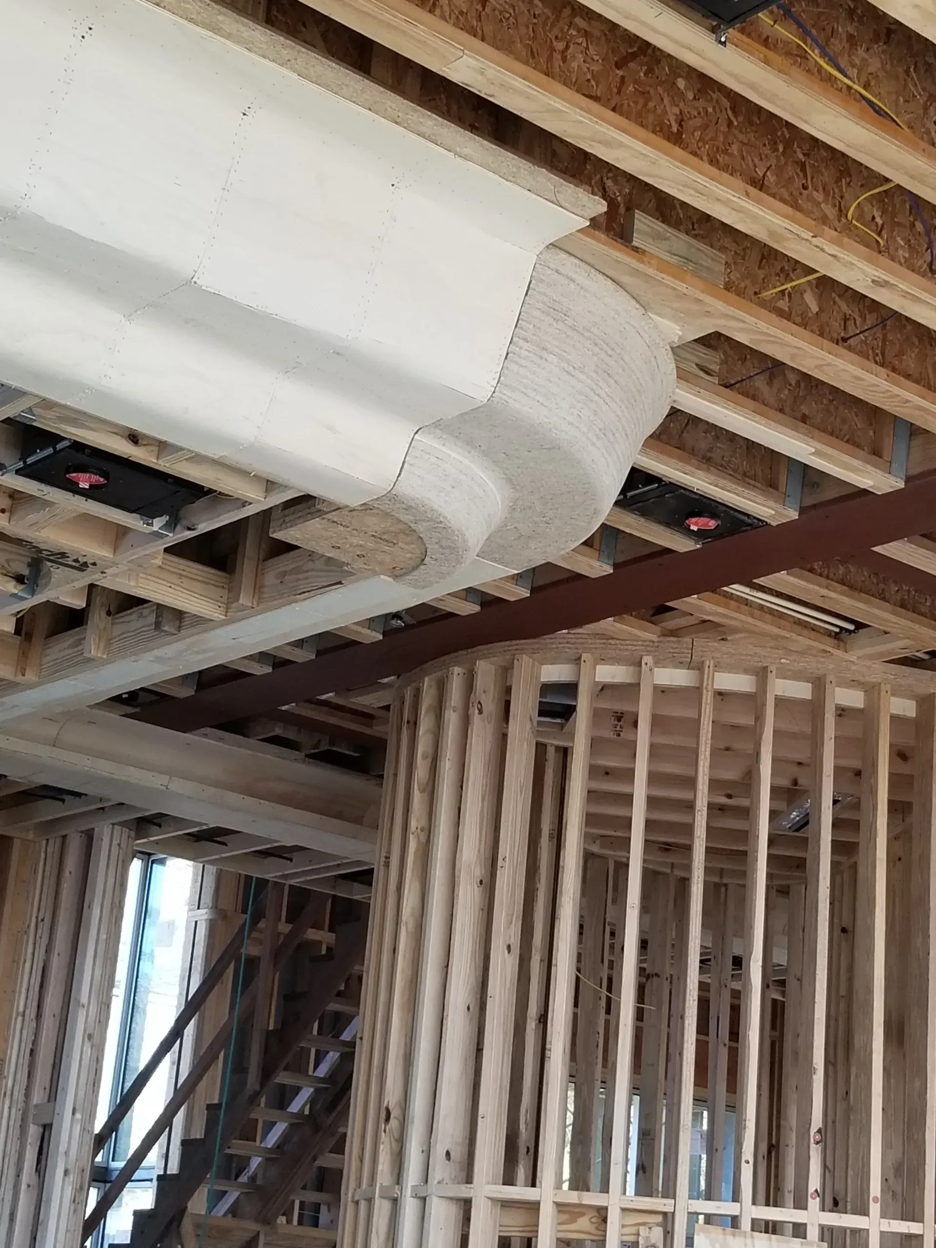 Unfinished interior framing with exposed ceiling joists and white ductwork in a construction site