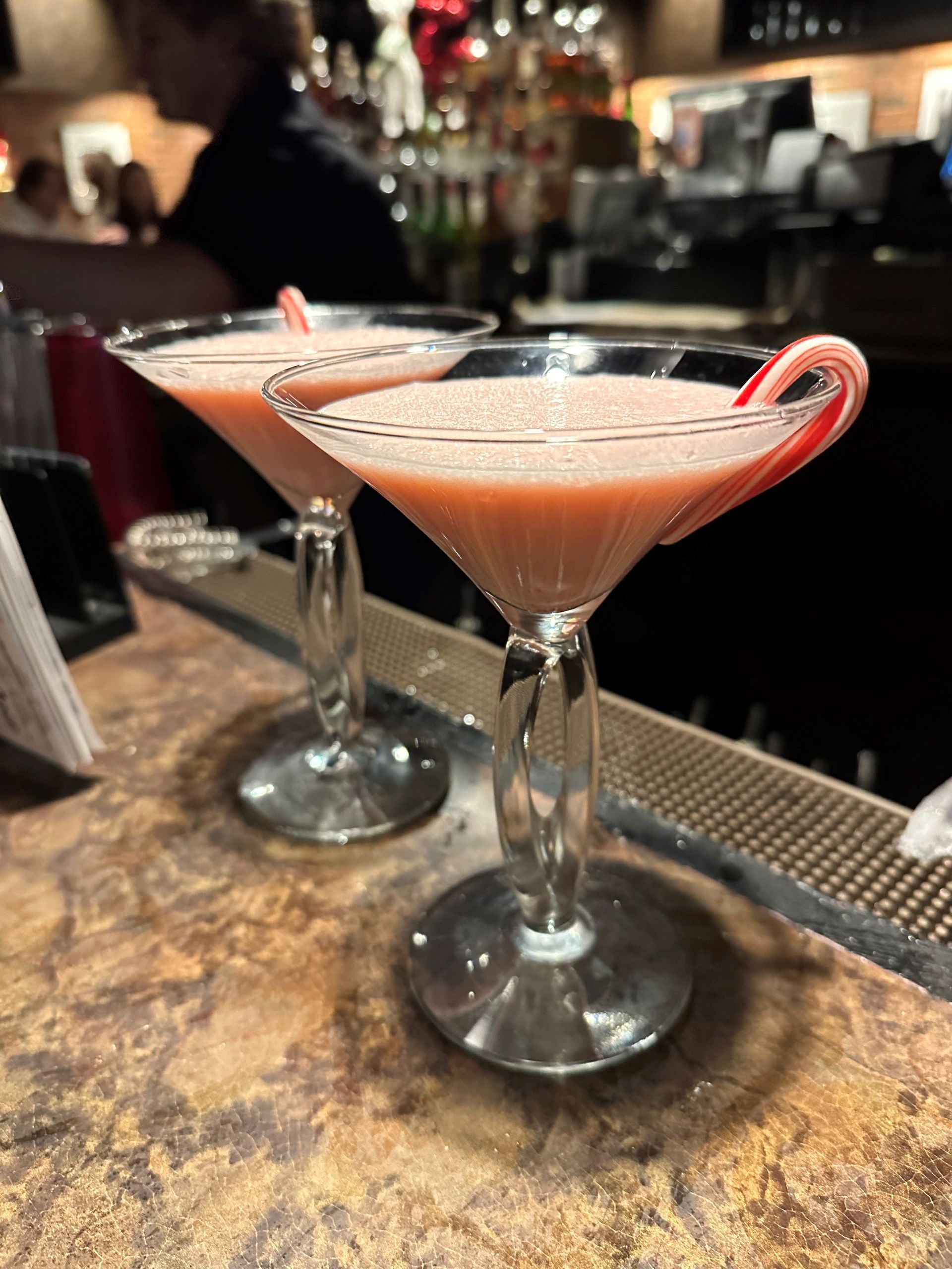 two martini glasses with candy canes in them on a bar .