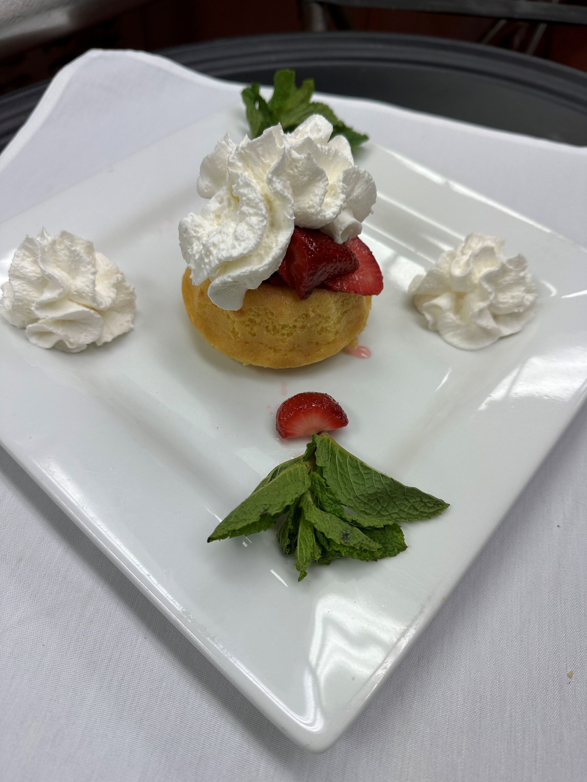 A white plate topped with a dessert with whipped cream strawberries and mint leaves.