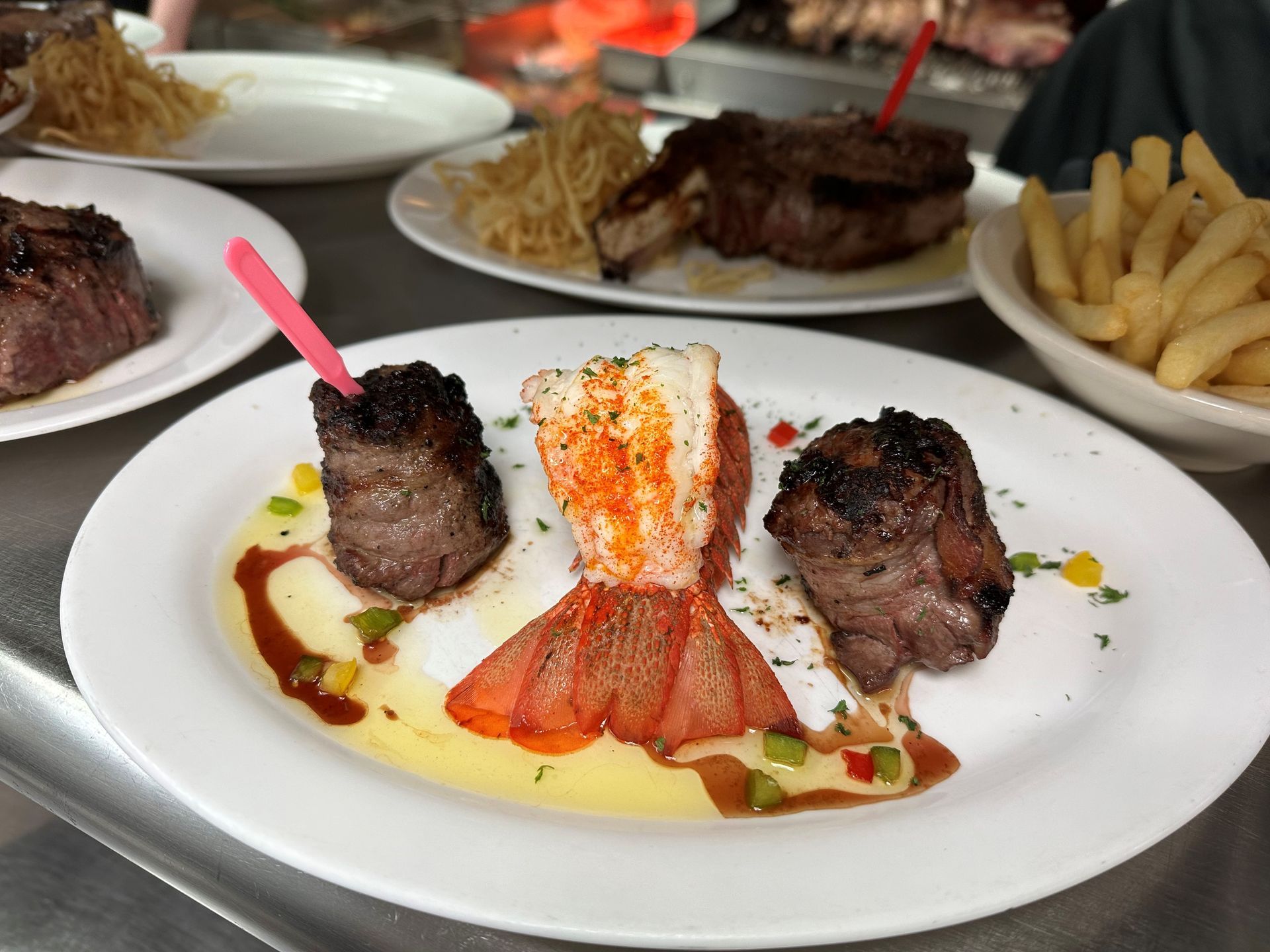 A white plate topped with meat and a lobster tail