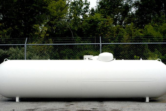 Large white propane tank in front of a chain-link fence and trees