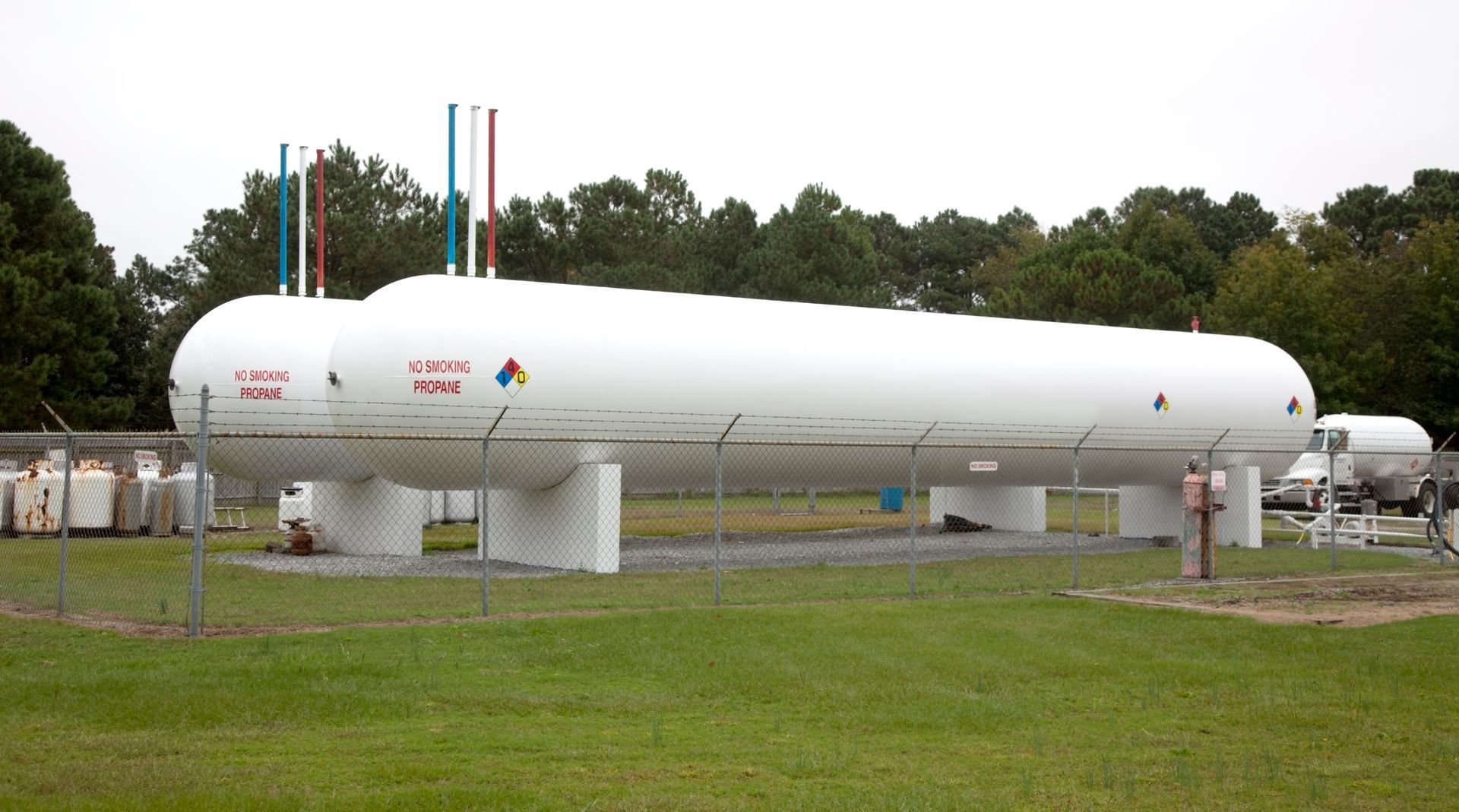 Large white cylindrical industrial tank on supports in a grassy field with trees behind it