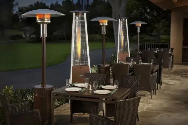 Outdoor restaurant patio with wicker tables and tall patio heaters at dusk
