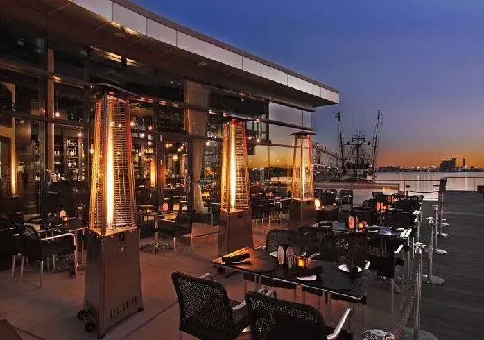 Outdoor restaurant patio at sunset with tables, chairs, and warm lights overlooking the water