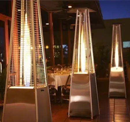 Outdoor patio with tall glowing patio heaters beside dining tables at night