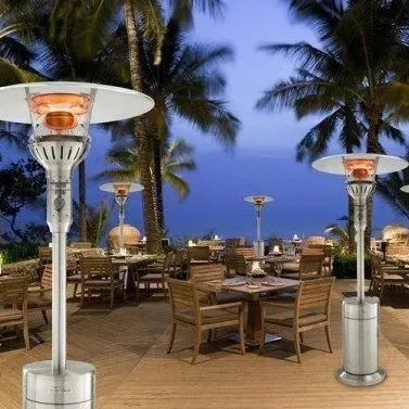 Outdoor patio dining area at dusk with palm trees and glowing heater lamps by the beach