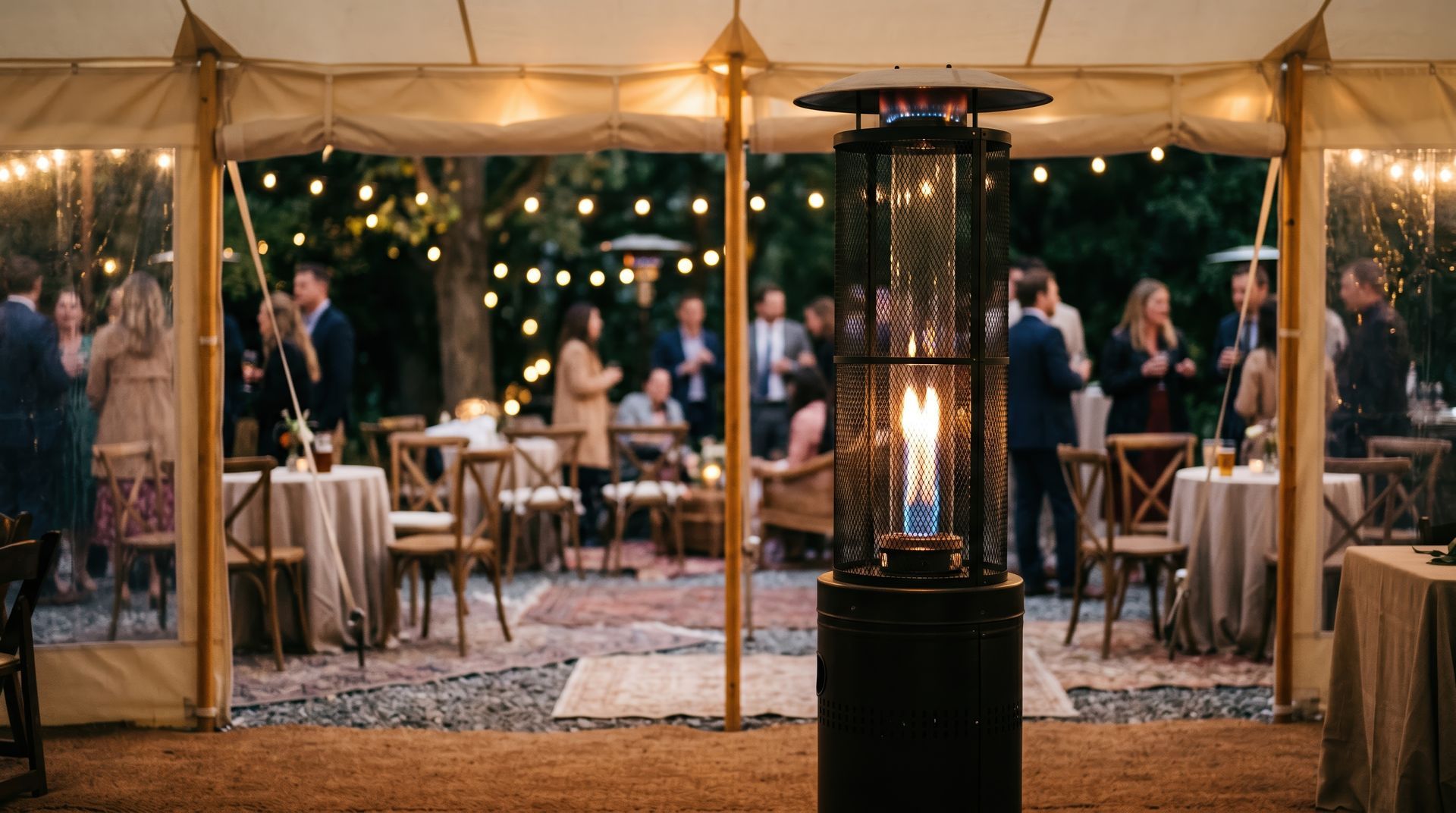 Evening tented outdoor reception with guests, tables, string lights, and a tall patio heater in the center