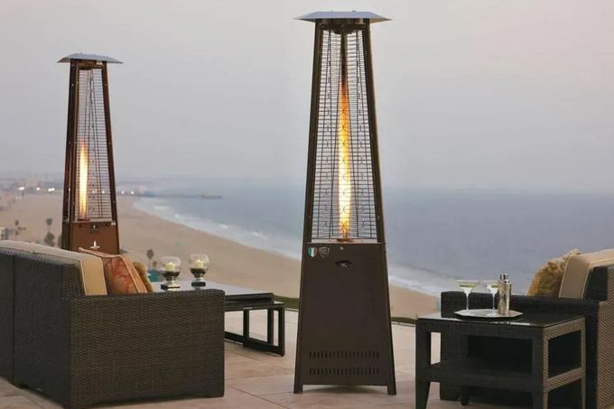 Seaside patio with wicker chairs, lit heaters, and a beach view at dusk