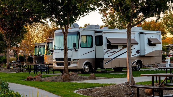 White RVs parked in a leafy campground beside picnic tables at dusk