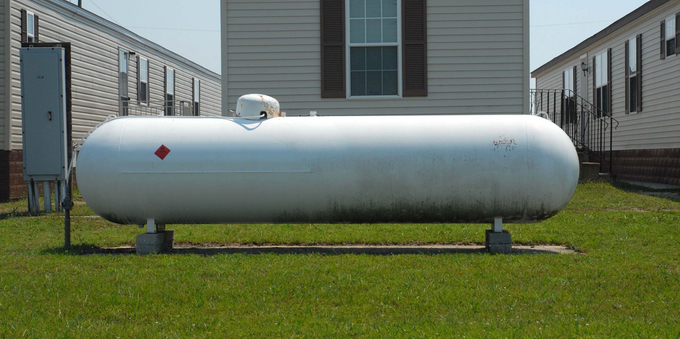White propane tank on a grassy lawn between two houses