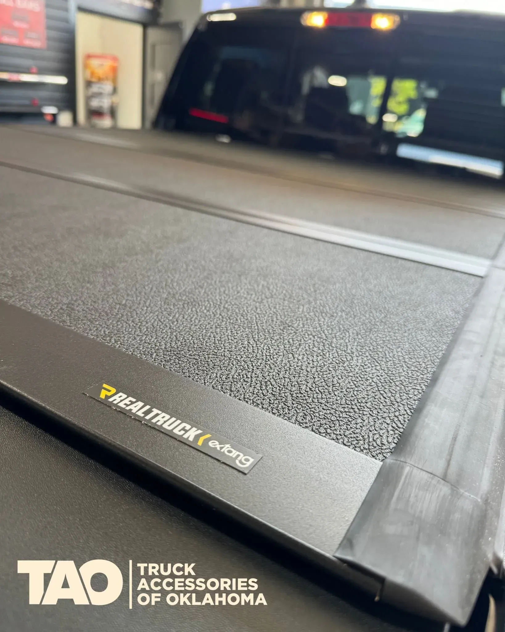 Black truck bed cover with textured surface and TAD Truck Accessories logo in foreground