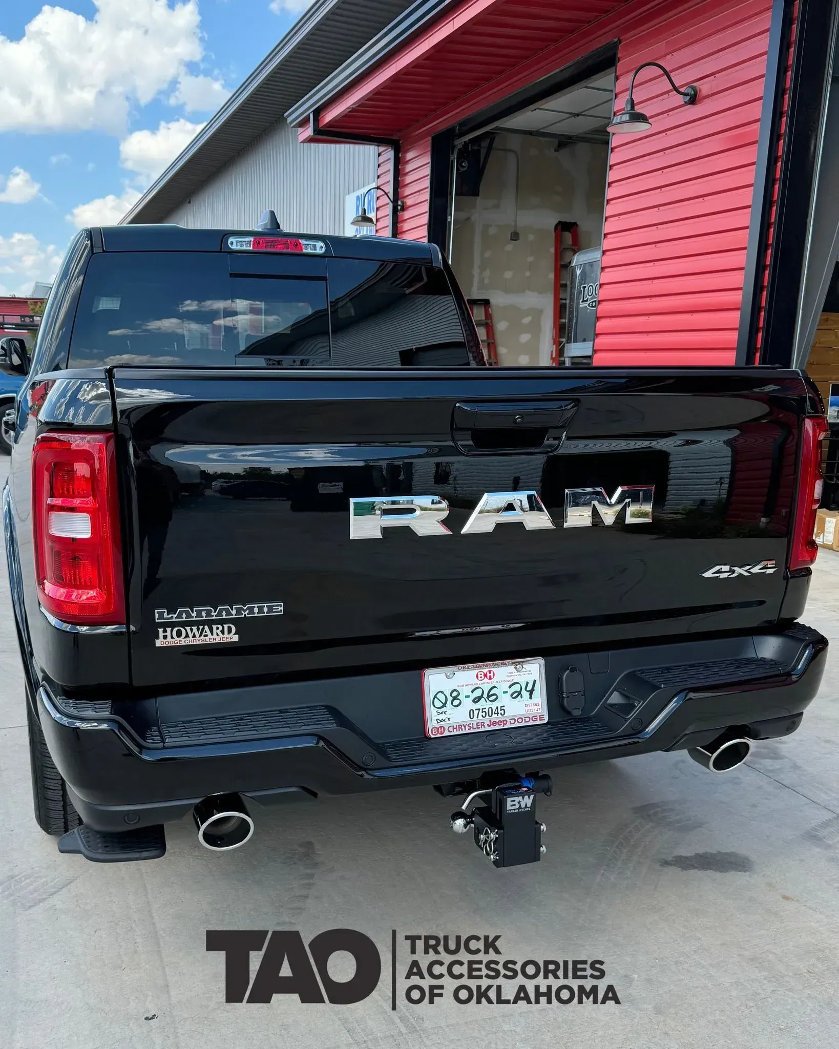 Black RAM pickup parked by a red building, rear view with truck accessories logo watermark.