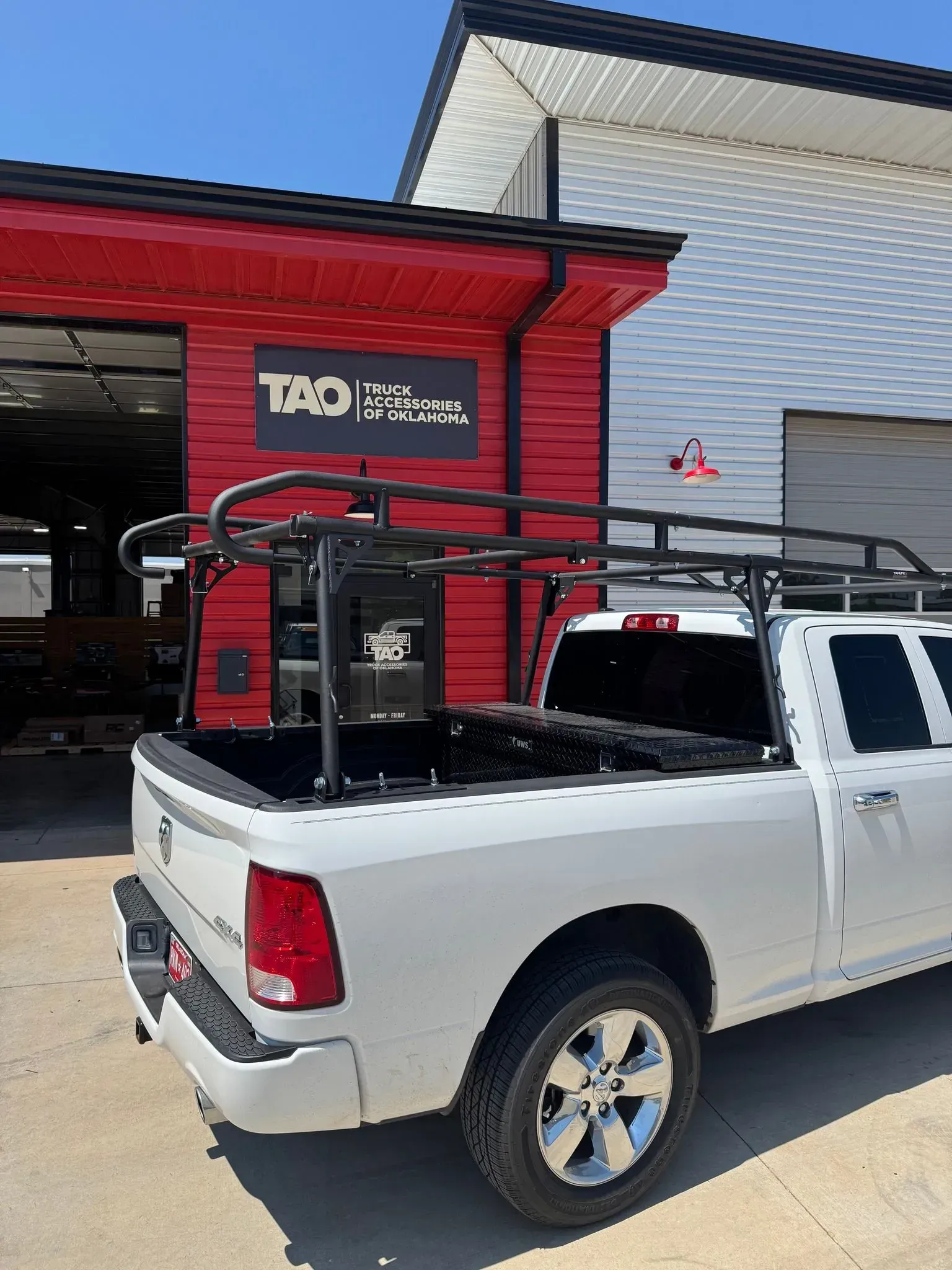 White pickup truck with a black roof rack parked outside a red-and-white storefront under a blue sky
