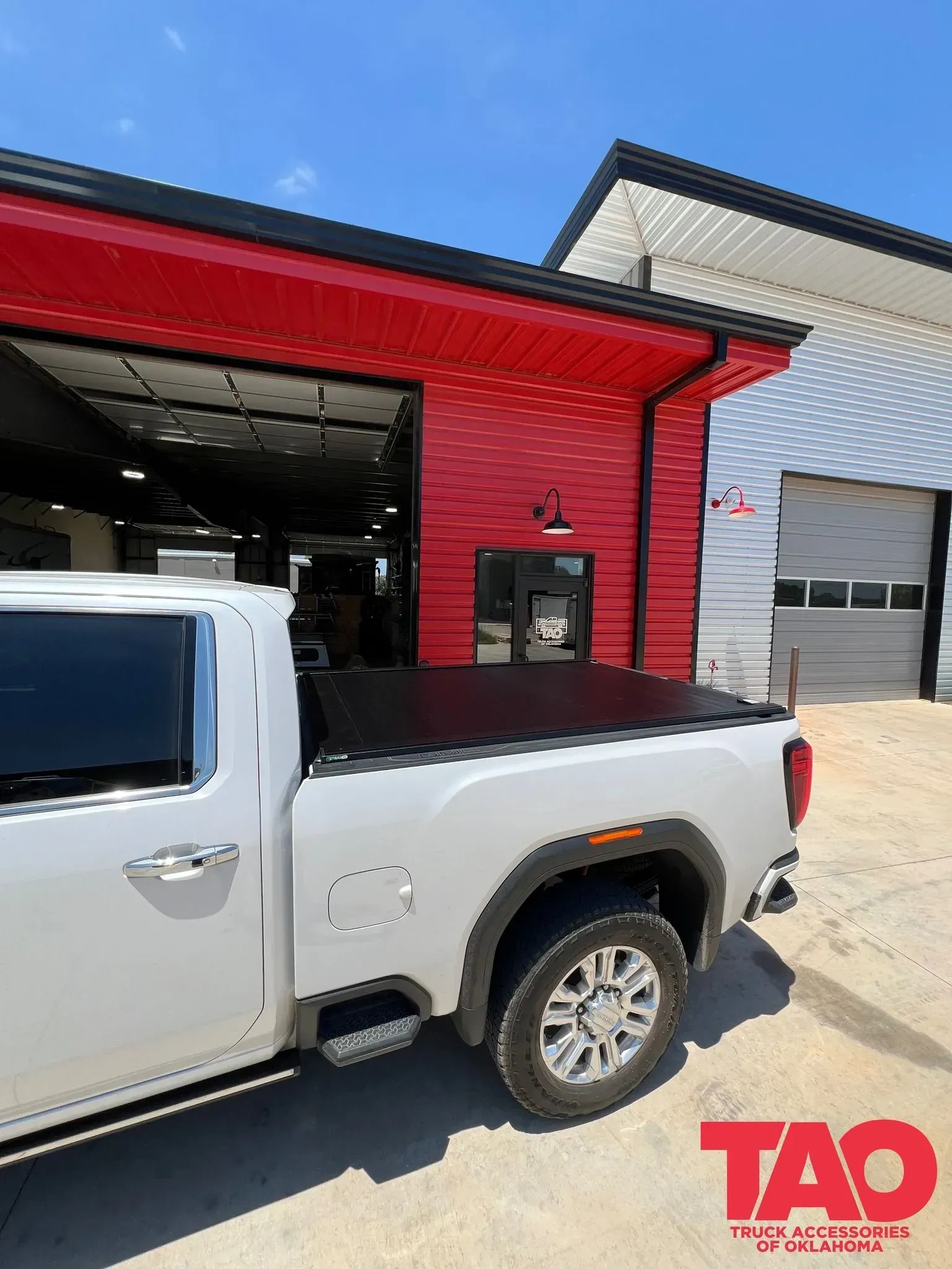 White pickup truck parked beside a red industrial garage with open service bay.