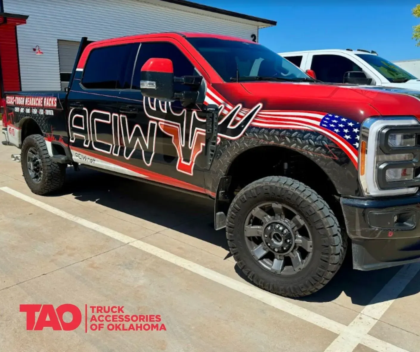 Red lifted black truck with red accents and large graphic wrap parked outside a building