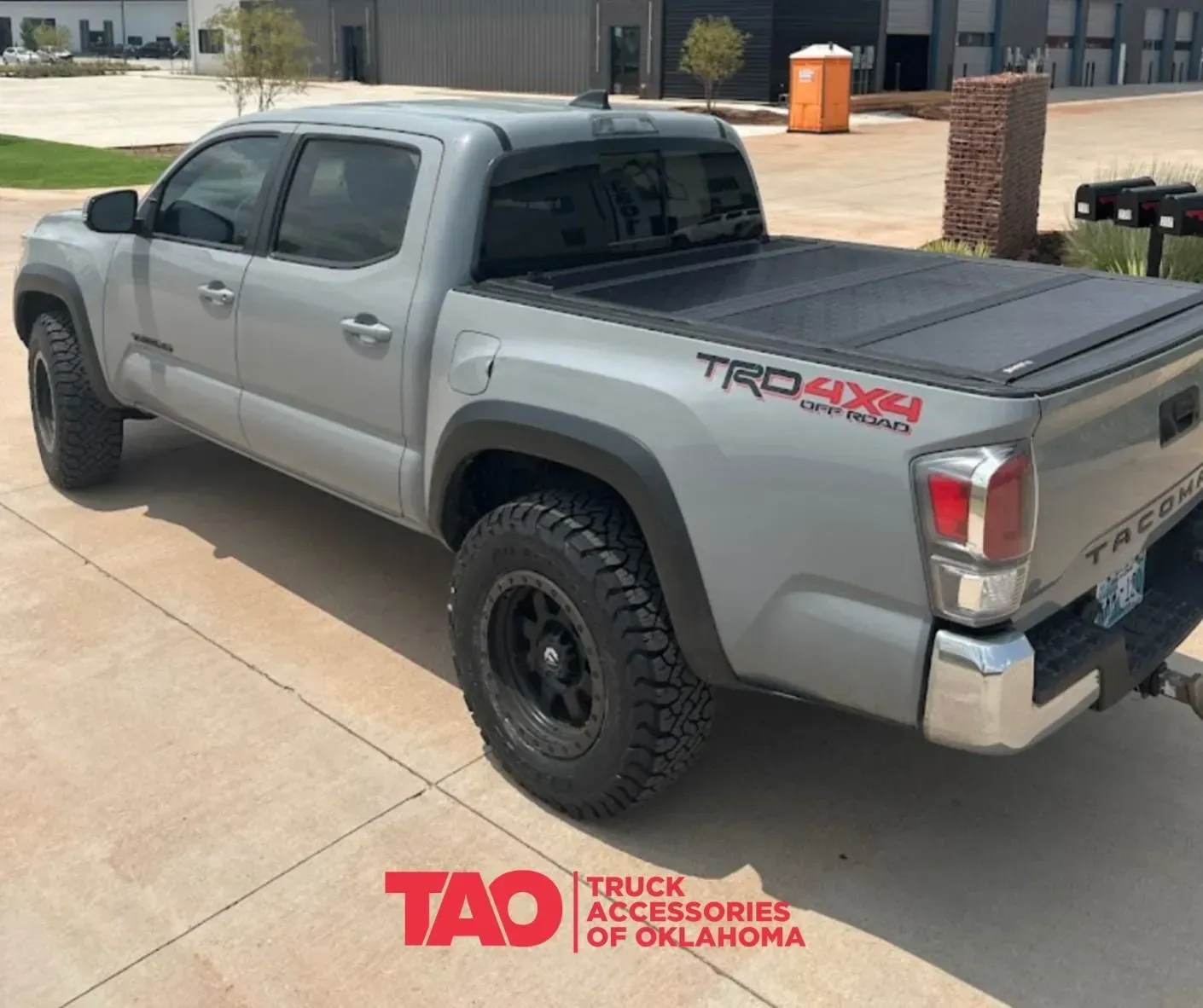 Silver Toyota Tacoma pickup with black off-road tires parked in a driveway, rear three-quarter view