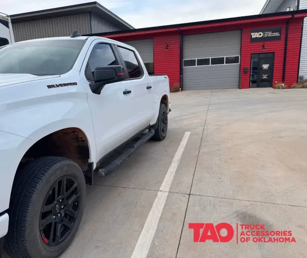 White pickup truck parked outside a red service garage with a black building and concrete lot