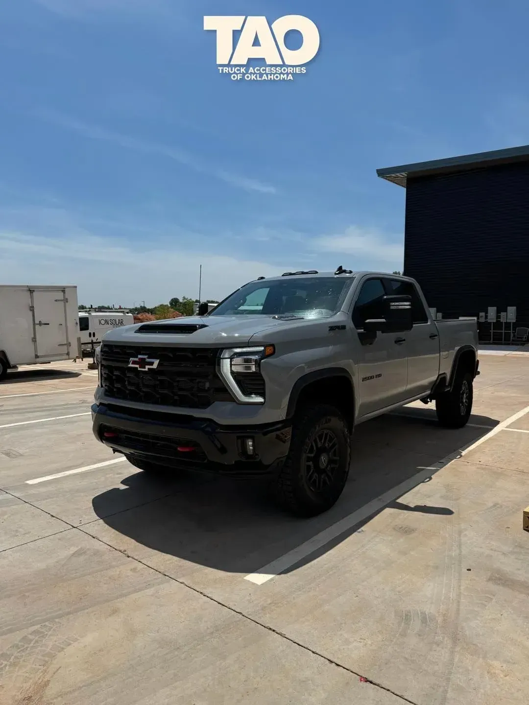 Gray pickup truck parked outside a warehouse on a sunny day.