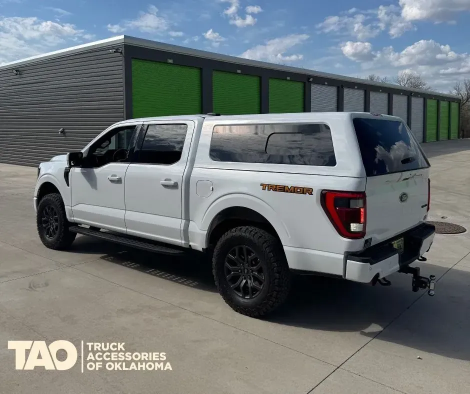 White pickup truck with camper shell parked outside green storage units under a blue sky