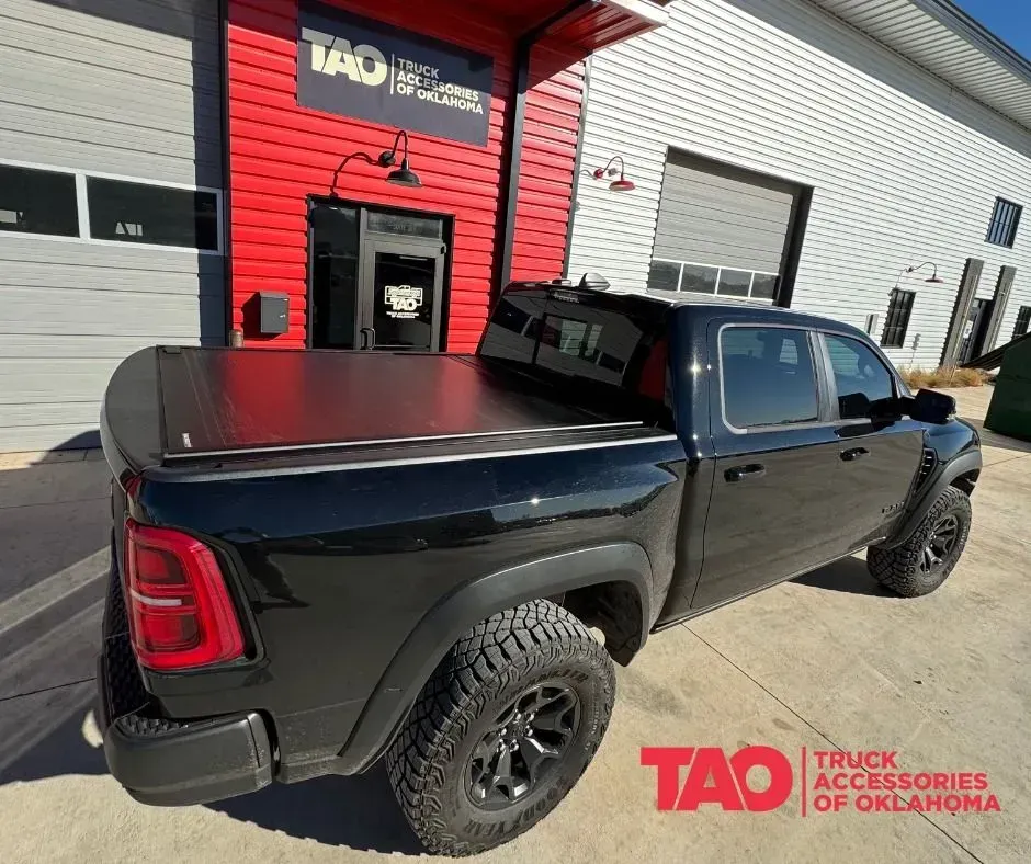Black pickup truck with a hard bed cover parked outside a truck accessories shop.