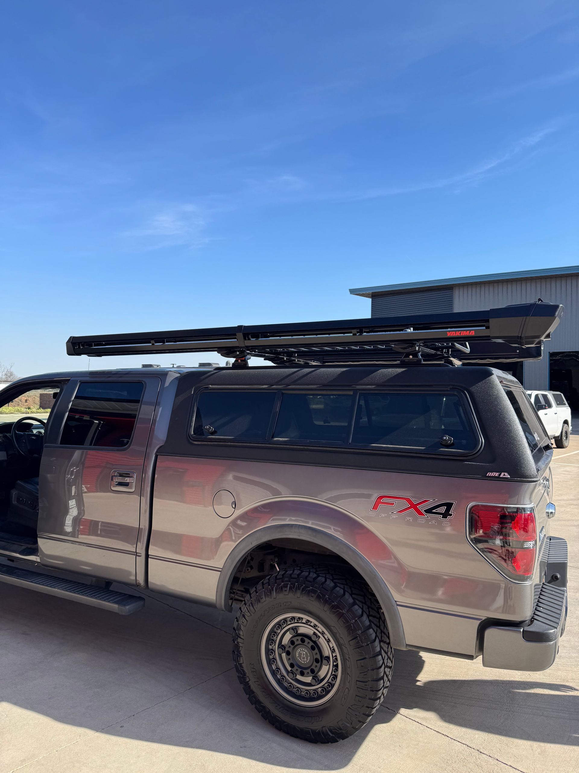 Silver pickup truck with roof rack and off-road tires parked beside a building under a blue sky