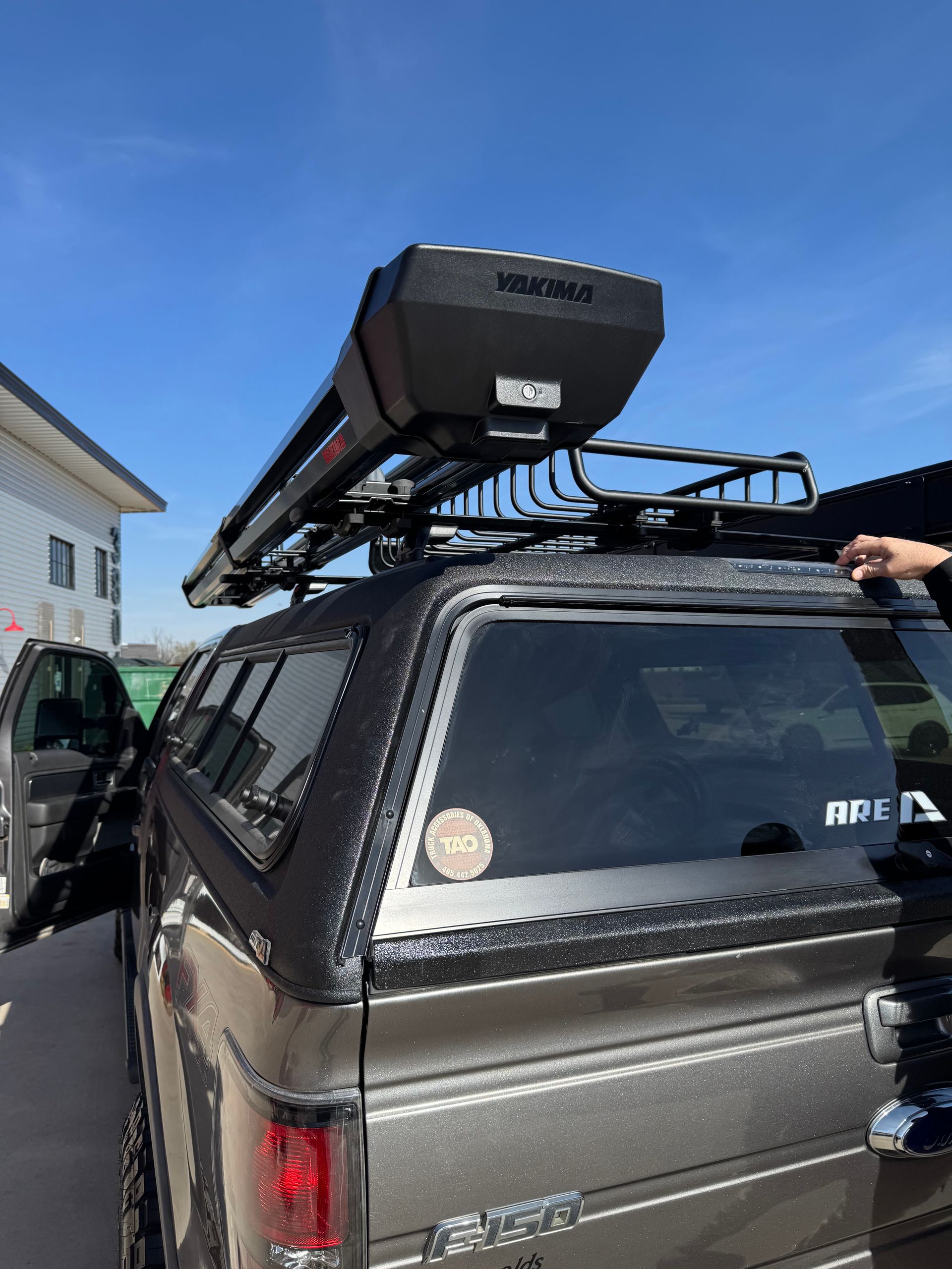 Pickup truck with ladder rack and roof cargo box parked outdoors under a blue sky