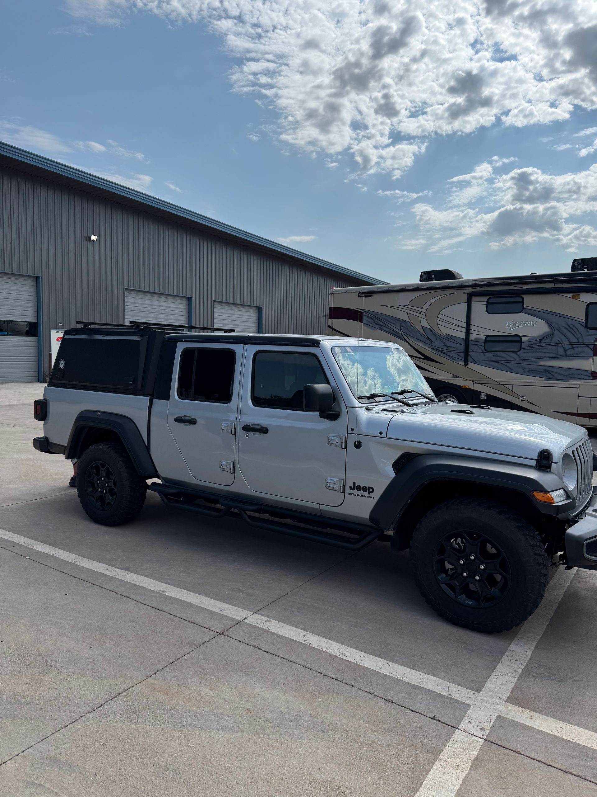 White off-road Jeep parked outside an industrial building under a partly cloudy sky