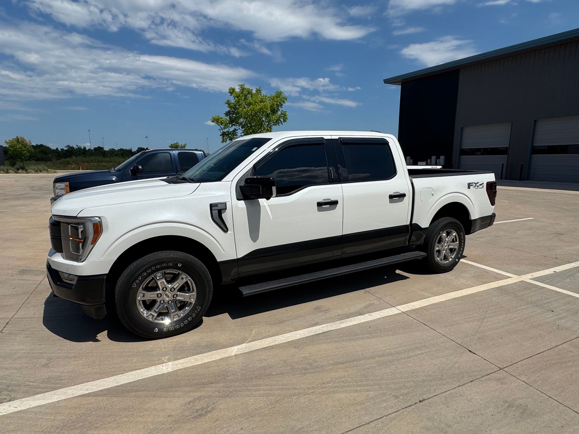White pickup truck parked in a lot beside a dark building under a blue sky.