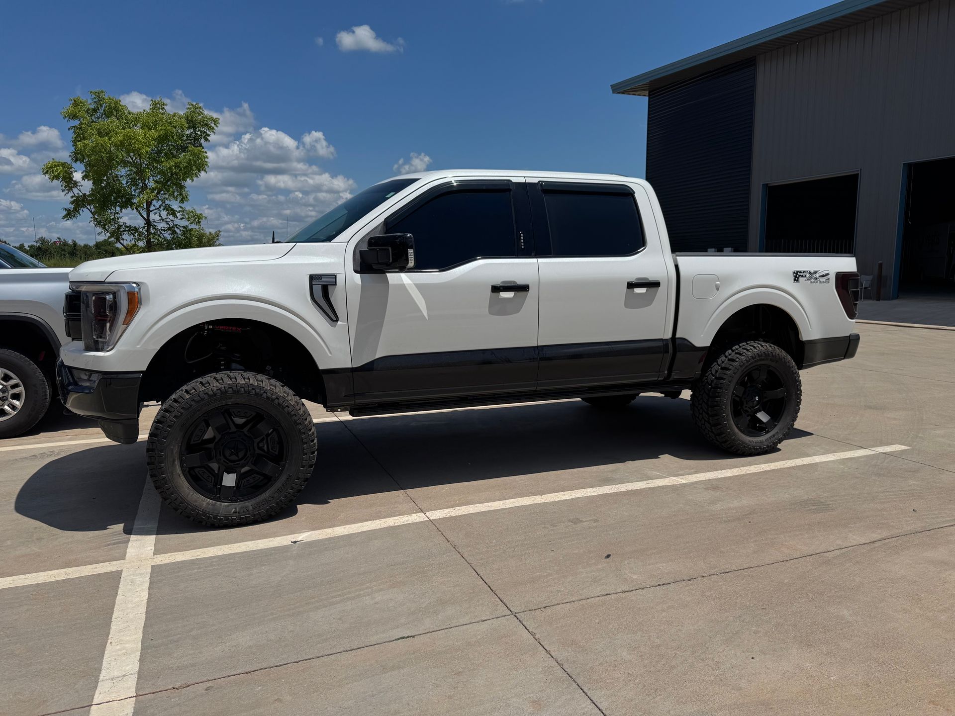 White lifted pickup truck parked beside a warehouse on a sunny day
