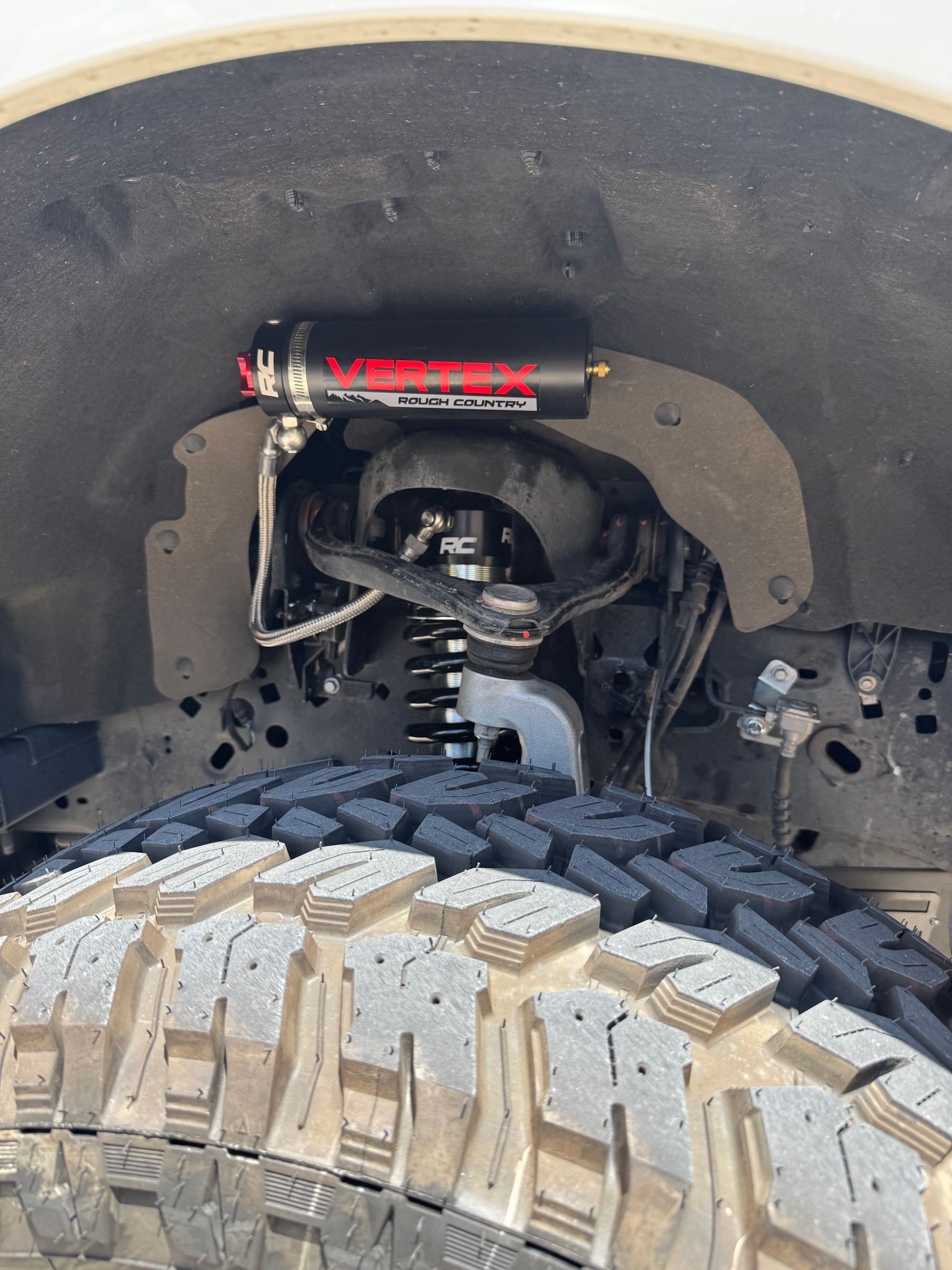 Off-road truck tire and suspension with visible red shock absorber inside wheel well