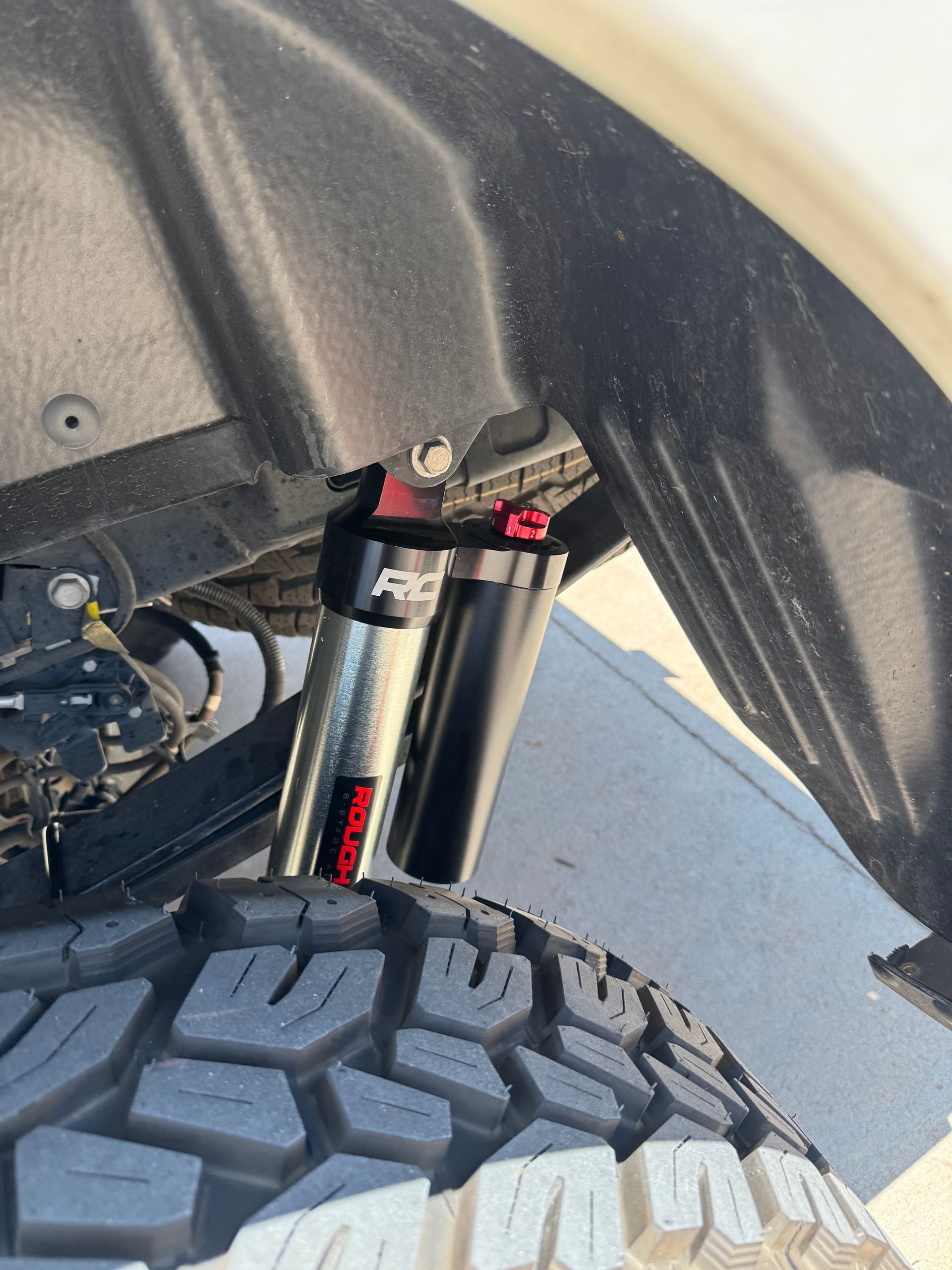 Close-up of a truck’s front tire and suspension under the wheel well, with off-road tread visible.