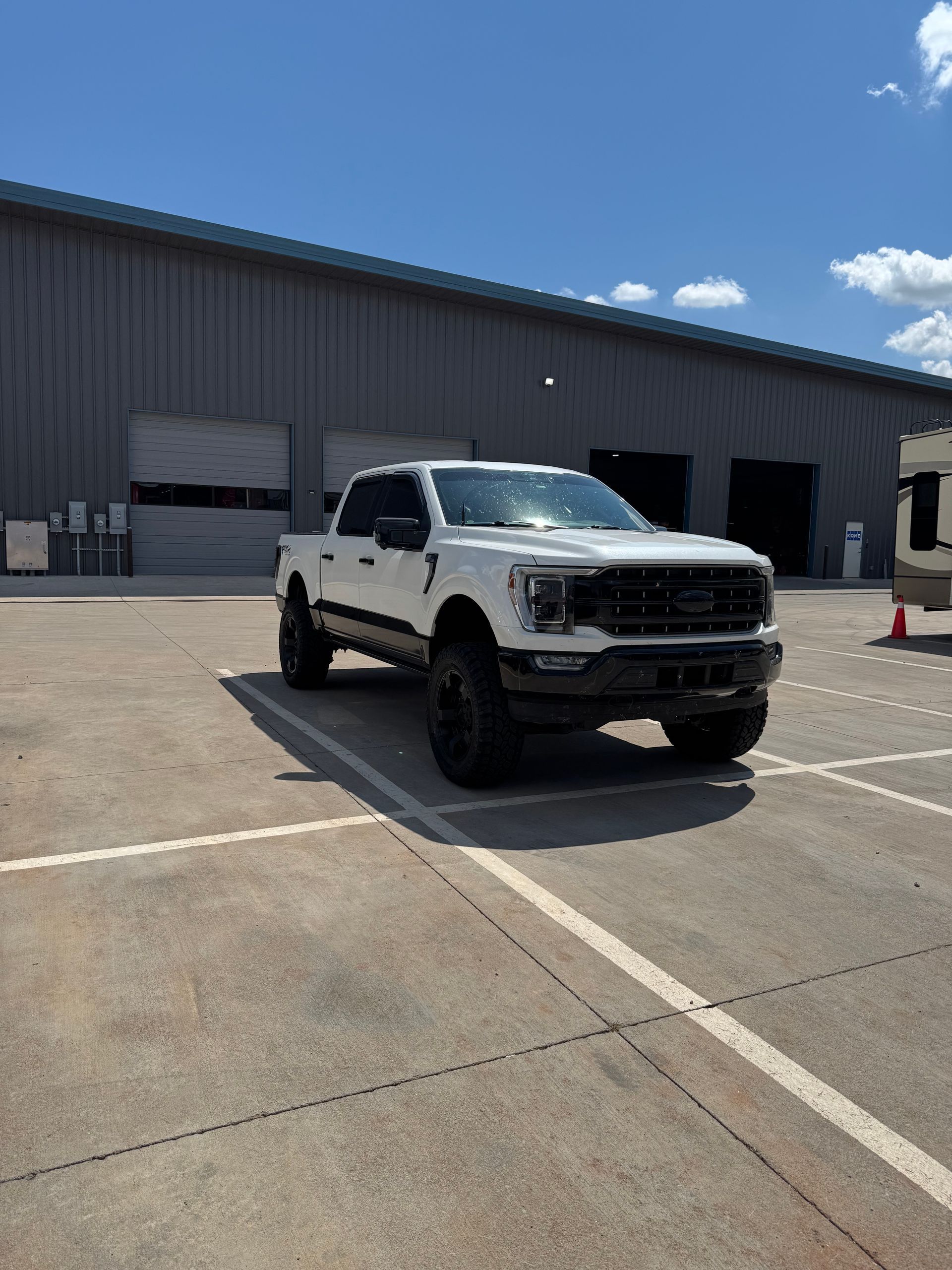 White lifted pickup truck parked in front of a warehouse under a bright blue sky