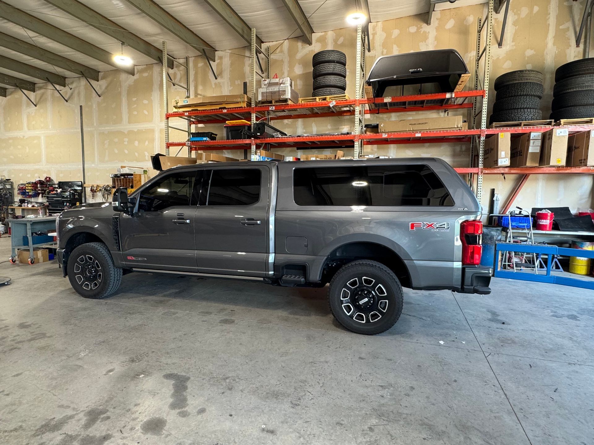 Gray pickup truck parked inside an auto shop with tires and equipment on shelves