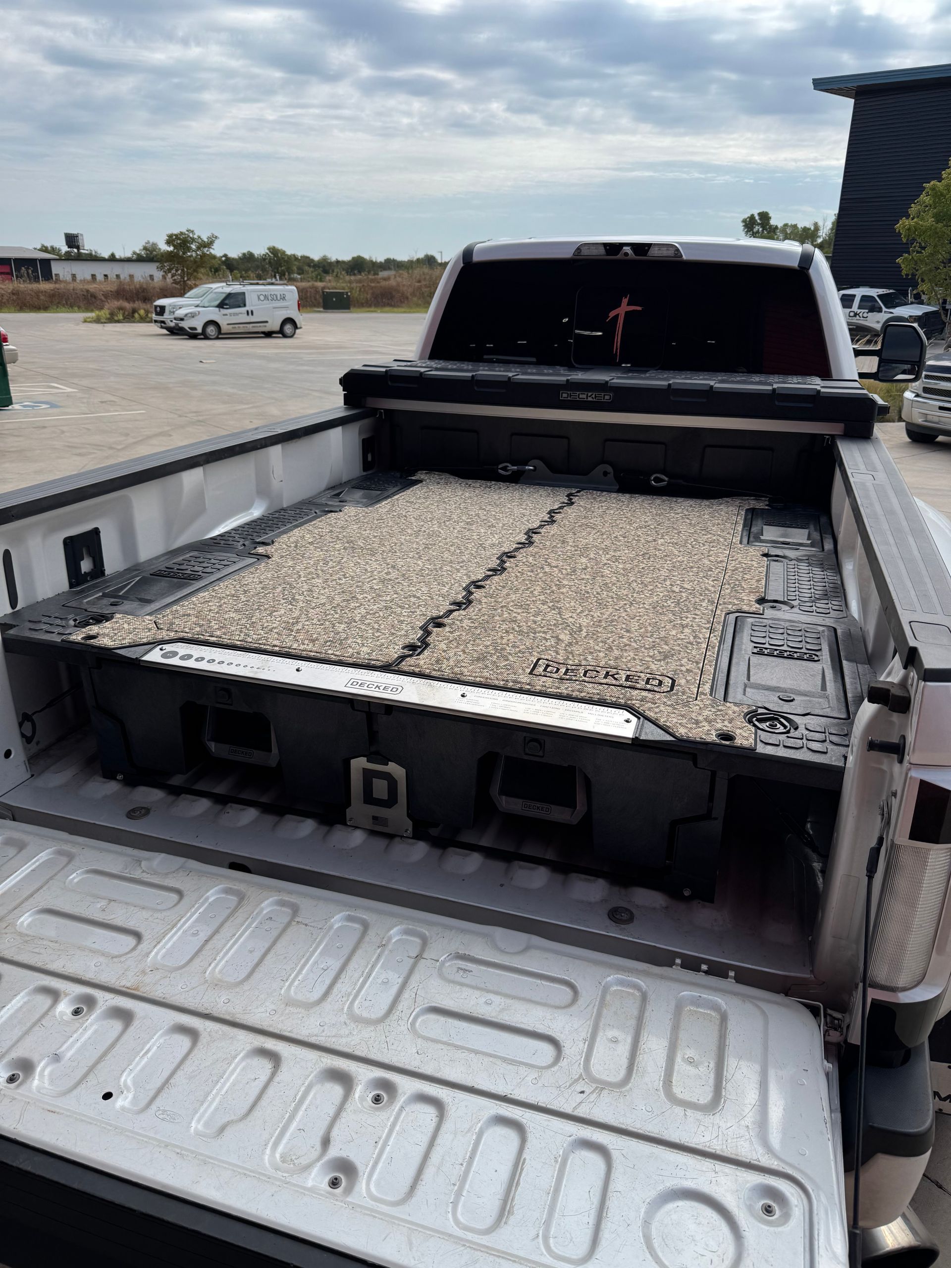 Pickup truck bed filled with pale gravel at a construction site, viewed from the tailgate.